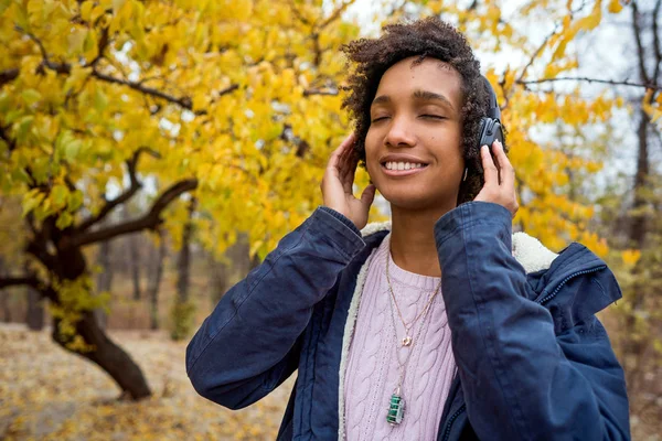 Beautiful african girl in autumn park listening to music outdoors smiling — Stock Photo, Image