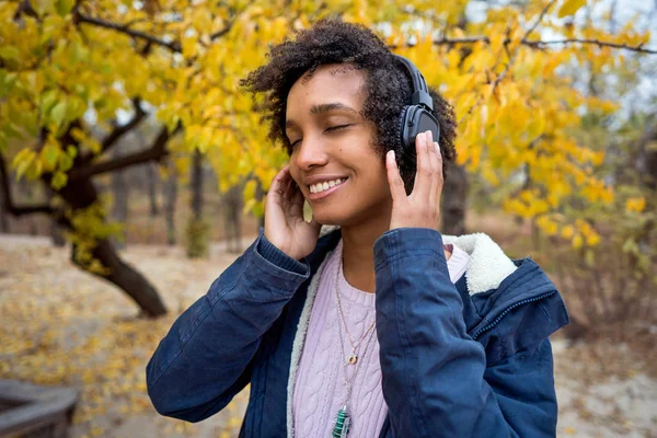 Sonbahar parkında güzel bir Afrikalı kız açık havada gülerek müzik dinliyor. — Stok fotoğraf