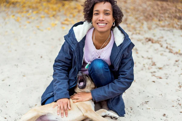 Beautiful african girl in autumn park on nature plays with a dog — Stock Photo, Image