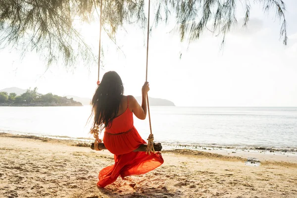 Дівчинка в червоній сукні на гойдалці серед тропічних пальм Таїланду після заходу сонця. — стокове фото