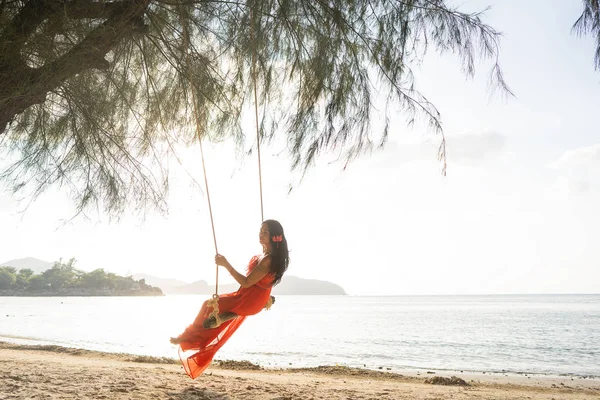 Meisje in een rode jurk op een schommel tussen tropische palmbomen in Thailand bij zonsondergang — Stockfoto