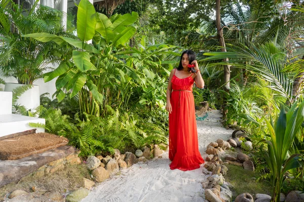 Menina em um vestido vermelho entre palmeiras tropicais na Tailândia ao pôr do sol — Fotografia de Stock