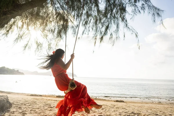 Meisje in een rode jurk op een schommel tussen tropische palmbomen in Thailand bij zonsondergang — Stockfoto