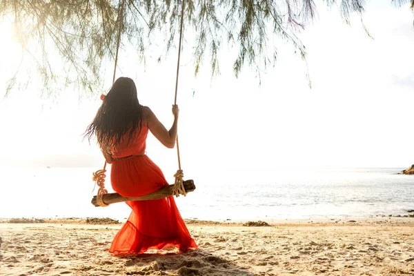 Ragazza in abito rosso su un'altalena tra le palme tropicali in Thailandia al tramonto — Foto Stock