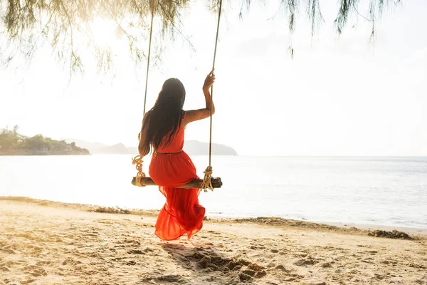 Meisje in een rode jurk op een schommel tussen tropische palmbomen in Thailand bij zonsondergang — Stockfoto