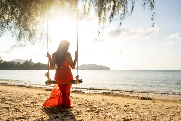 Meisje in een rode jurk op een schommel tussen tropische palmbomen in Thailand bij zonsondergang — Stockfoto