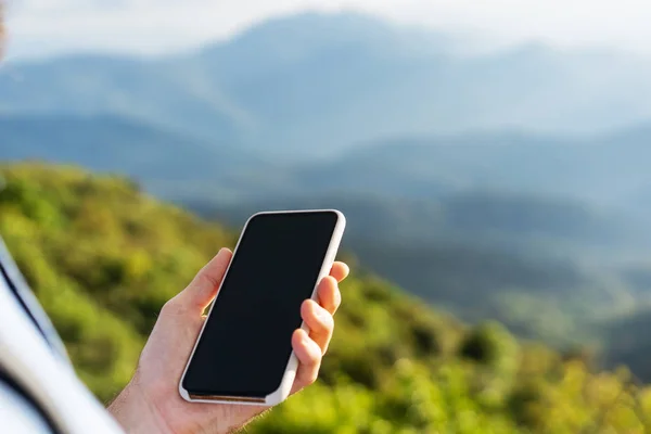 Homem segurando um telefone nas montanhas ao pôr do sol — Fotografia de Stock