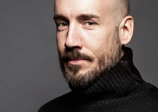 Fashion Portrait of a 40-year-old man standing over a light gray background in a black sweater. Close up. Classic style. Bald shaved head. Copy-space. Studio shot