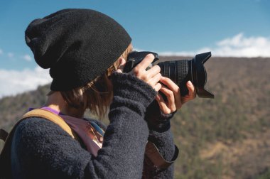 Yakın çekim portre sarışın kızla dağlarda fotoğraf çekimi bir dijital Slr fotoğraf makinesi. Şık freelance fotoğrafçı dağ beyaz gezi sırt çantası ile