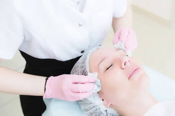 Um close-up do procedimento de limpeza no escritório de cosmetologia. As mãos do cosmetologista em luvas rosa são removidas do rosto de uma jovem com uma esponja limpando a máscara. — Fotografia de Stock