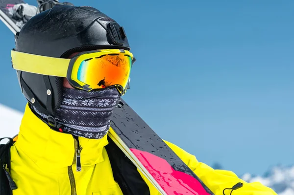 Um retrato de perto de um esquiador em um capacete protetor e óculos é uma máscara e um lenço com esquis em seu ombro nas montanhas cobertas de neve do Cáucaso. Esqui , — Fotografia de Stock