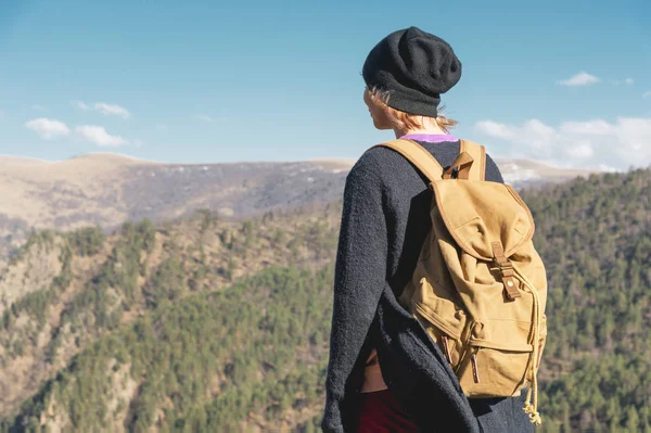 Un fotografo di viaggio ragazza hipster in un cappello e con uno zaino in piedi su una roccia e guardando le colline . — Foto Stock