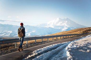 Güneş gözlüğü vintage bir sırt çantası ile şık bir sakallı hippi güneşli bir günde asfalt yolda yürür. Otostop ve hiking kavramı.