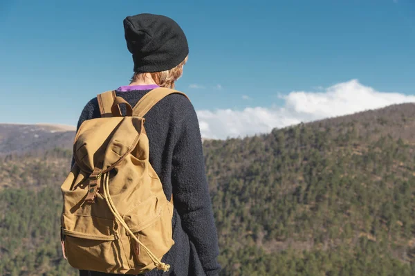 Uma fotógrafa de viagem hipster em um chapéu e com uma mochila em pé sobre uma rocha e olhando para as colinas . — Fotografia de Stock