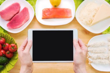 Tasarım iş parçası. Eller bir tablet Pc ham deniz ürünleri içeren bir tablo üzerinde peynir ve sebze tutun. Gıda konu sunumu için boş ekran