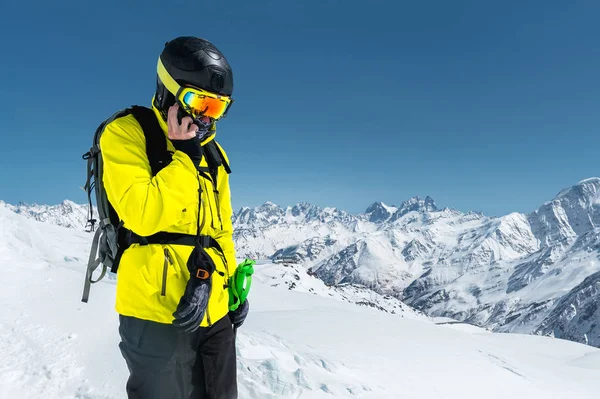 Retrato de um atleta esquiador usando um capacete e uma máscara falando no telefone alto nas montanhas do Cáucaso, onde em torno da neve — Fotografia de Stock