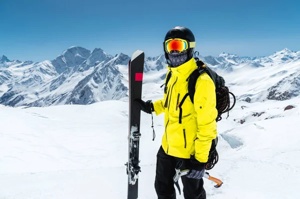 Närbild porträtt av en skidåkare som bär en skyddande hjälm och glasögon. Mask och halsduk med en isyxa i händerna bredvid skidor på de snöklädda bergen i Kaukasus. Skidåkning — Stockfoto