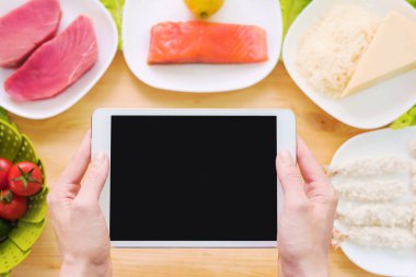 Tasarım iş parçası. Eller bir tablet Pc ham deniz ürünleri içeren bir tablo üzerinde peynir ve sebze tutun. Gıda konu sunumu için boş ekran