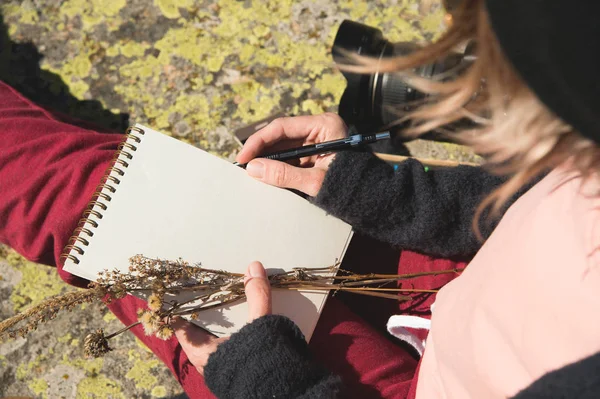 Primer plano en las manos de una chica sosteniendo un cuaderno en blanco. Un ramo seco de hierbas en la mano y un lápiz. Diseñador de viajes artista — Foto de Stock