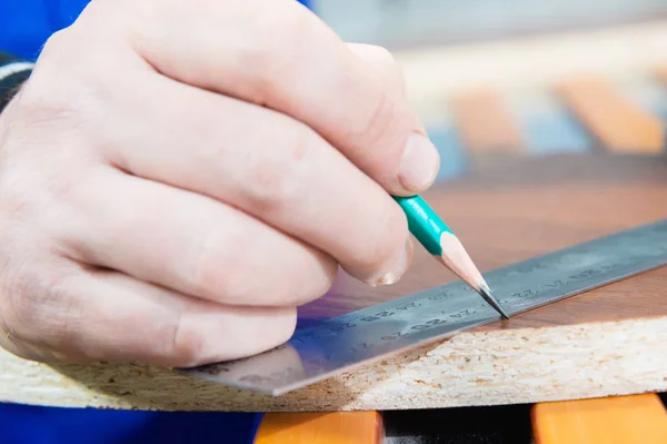 Close-up of the hand of the carpenters master is marked with a ruler and a pencil blank. The concept of manual furniture production