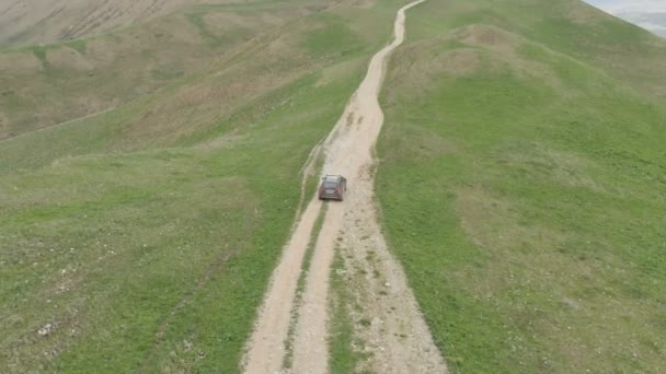 The off-road car rides along a mountain road against the backdrop of mountains and plateaus in the evening. The video is shot on Mavik Air 4k 100mbps — Stock Video