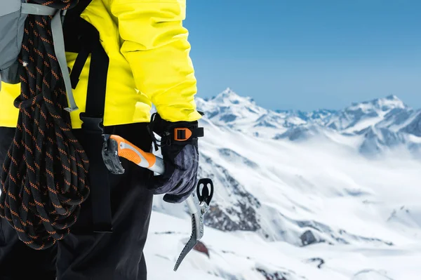 Un alpinista tiene una piccozza alta sulle montagne innevate. Primo piano da dietro. sport all'aperto estremi di arrampicata all'aperto con attrezzature alpinistiche — Foto Stock