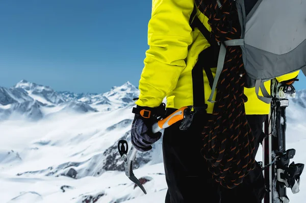 A mountaineer man holds an ice ax high in the mountains covered with snow. Close-up from behind. outdoor extreme outdoor climbing sports using mountaineering equipment
