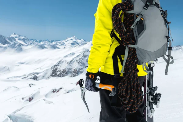 Um homem montanhista segura um machado de gelo nas montanhas coberto de neve. Close-up por trás. esportes de escalada ao ar livre extremos ao ar livre usando equipamentos de alpinismo — Fotografia de Stock