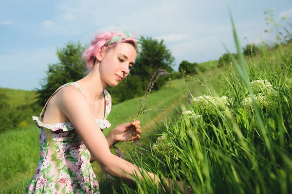 Retrato de una joven linda chica feliz con cabello multicolor recoge flores junto a un camino rural al atardecer. El concepto de armonía humana con la naturaleza de la primavera y la felicidad — Foto de Stock