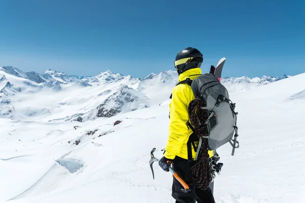 Horolezec muž drží sekeru ice vysoké hory pokryté sněhem. Pohled z zad. extrémní venkovní horolezecké sportovní použití horolezeckého vybavení — Stock fotografie