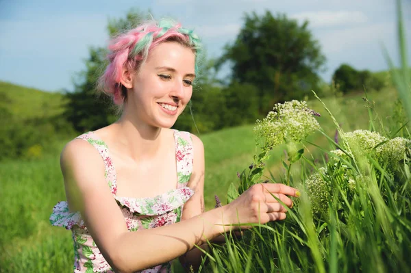 Retrato de uma jovem menina bonita feliz com cabelo multi-colorido recolhe flores ao lado de uma estrada rural ao pôr do sol. O conceito de harmonia humana com a natureza da primavera e da felicidade — Fotografia de Stock