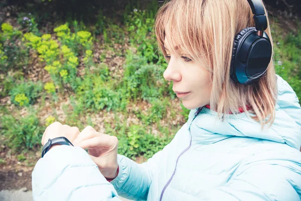 Portret młodego fitness kobieta ogląda jej inteligentny zegarek podczas przerwy szkolenia sportowego. Sportsmenka sprawdzanie impuls fitness inteligentny zegarek urządzenia w lesie. — Zdjęcie stockowe