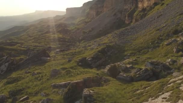 Una vista desde arriba sobre un valle esparcido con enormes piedras al pie de un alto acantilado. Un panorama al atardecer del Cáucaso con un giro. Revisión del lugar épico en 4k 100mbps — Vídeo de stock