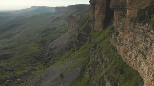 Vuelo a lo largo de los acantilados rocosos al pie de los acantilados épicos de la meseta en el Cáucaso Norte. Fotografía aérea Vuelo sobre campos verdes esparcidos con piedras en 4k 100mbps — Vídeos de Stock