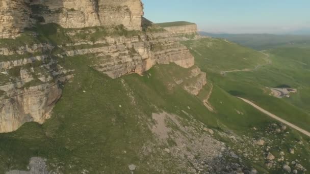 AERIAL: Voo sobre um penhasco alto, revelando uma vista da passagem na Rússia no norte do Cáucaso. Fotografia aérea da estrada no pôr do sol. Voo ao lado da rocha — Vídeo de Stock