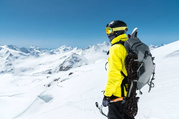 Een bergbeklimmer man houdt een ice ax hoog in de bergen bedekt met sneeuw. Uitzicht vanaf de achterkant. Outdoor extreme klimmen buitensporten met behulp van bergbeklimmen apparatuur — Stockfoto
