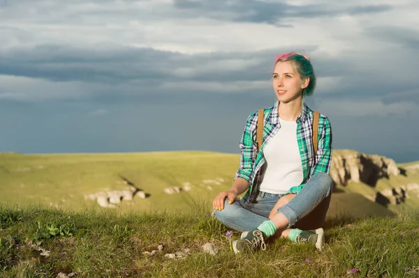 Retrato de jovem mulher sorridente viajante com cabelo multi-colorido. Sentado no alto das montanhas à noite com um declínio no fundo de um planalto — Fotografia de Stock