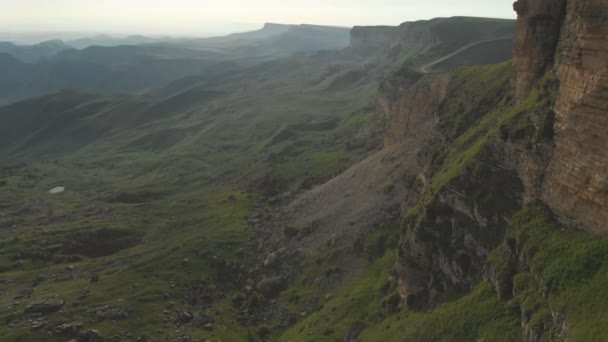 Vuelo a lo largo de los acantilados rocosos al pie de los acantilados épicos de la meseta en el Cáucaso Norte. Fotografía aérea Vuelo sobre campos verdes esparcidos con piedras en 4k 100mbps — Vídeos de Stock