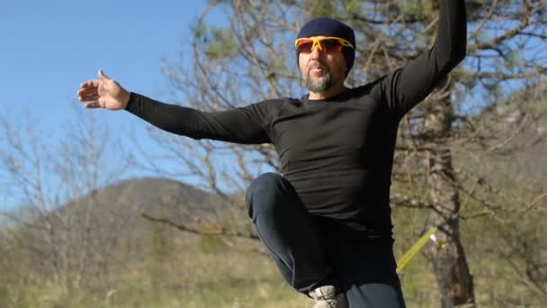 Een man gekleed in een hoed en baard, close-up opstaat om te lopen in de wind tegen de achtergrond van de bergen van de Kaukasus van de blauwe lucht en de wolken — Stockvideo
