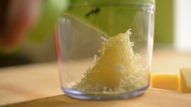 Une jeune fille frotte du fromage dans une râpe mécanique spéciale avec un verre transparent sur une table en bois — Video