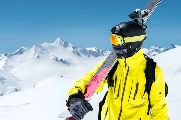 Um retrato de um esquiador em um capacete protetor e óculos é uma máscara e um lenço com esquis em seu ombro nas montanhas cobertas de neve do Cáucaso. Esqui , — Fotografia de Stock