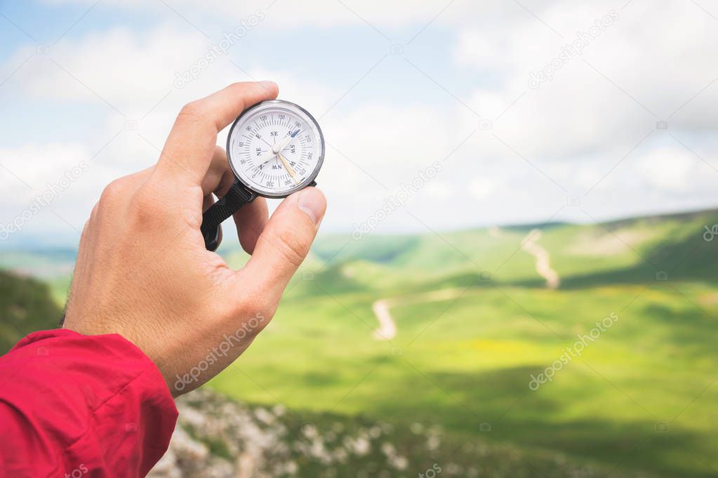 A mans hand of a tourist with an authentic compass on the background of a mountain road landscape
