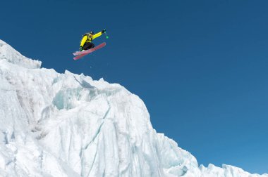 Bir mavi gök yüksek dağlarda karşı bir buzul üzerinden atlama atlama bir kayakçı. Profesyonel kayak