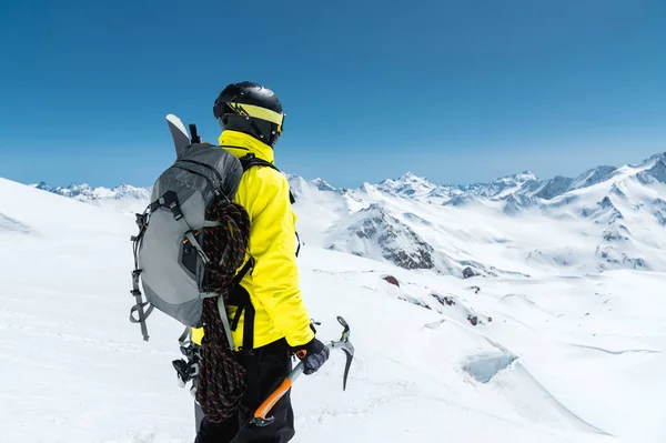 Een bergbeklimmer man houdt een ice ax hoog in de bergen bedekt met sneeuw. Uitzicht vanaf de achterkant. Outdoor extreme klimmen buitensporten met behulp van bergbeklimmen apparatuur — Stockfoto