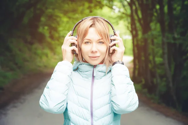 Portret pięknej, młodej kobiety, trzymając słuchawki słuchać muzyki na zewnątrz w lesie. Radosna muzyka — Zdjęcie stockowe