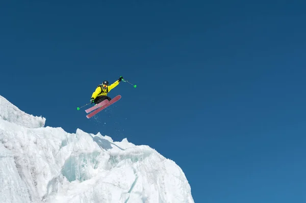 Ένα άλμα σκιέρ πηδώντας από έναν παγετώνα ενάντια σε ένα καταγάλανο ουρανό ψηλά στα βουνά. Επαγγελματίες σκι — Φωτογραφία Αρχείου