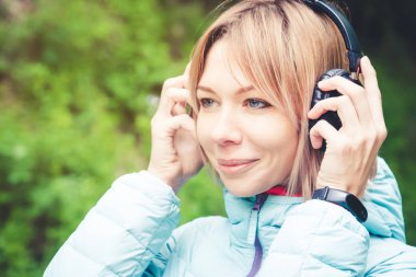 Müzik açık havada ormandaki kulaklık tutan güzel bir genç kadın portresi kapatın. Neşeli müzik