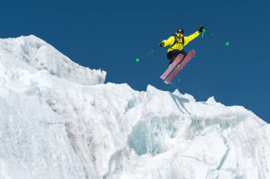Bir mavi gök yüksek dağlarda karşı bir buzul üzerinden atlama atlama bir kayakçı. Profesyonel kayak