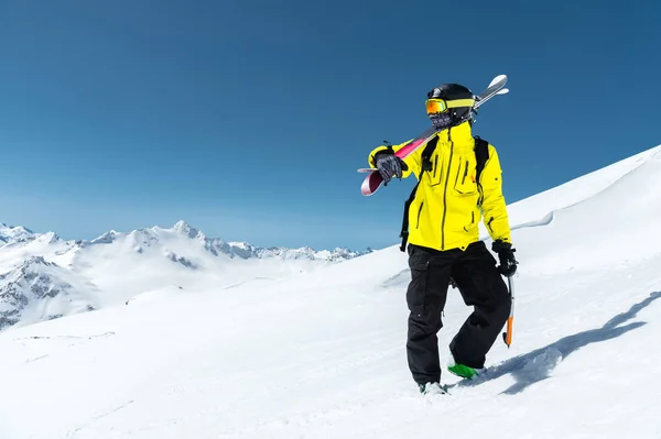 Das Porträt eines Skifahrers mit Schutzhelm und Brille ist eine Maske und ein Schal mit Skiern auf der Schulter in den schneebedeckten Bergen des Kaukasus. Skifahren, — Stockfoto