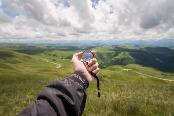 A mans hand of a tourist with an authentic compass on the background of a mountain road landscape — Stock Photo, Image